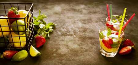 Two glasses of cold lemonade with mint, strawberry and lime on dark background. Toned.の写真素材
