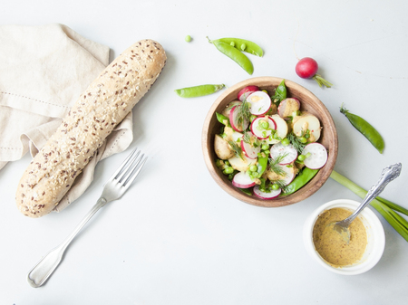 A wooden bowl of spring vegetable salad with mustard dressing on grey background. Minimal.