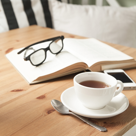 Composition with tea cup, book, and mobile phone on a wooden table.の写真素材