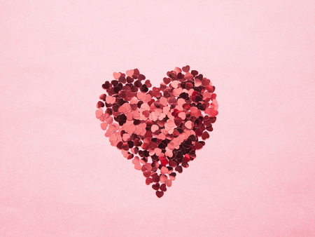 Heart shape made of small glittering hearts on pink background. Concept for love, romantic and Valentine's day. Flat lay.の写真素材