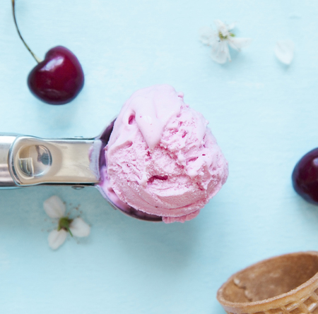 Cherry ice cream scoop in spoon, empty sugar cone, cherry berry and flowers on blue background....
