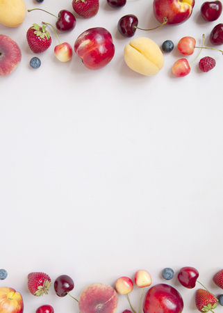 Variety of fresh juicy berries and fruits on grey background. Minimal food frame. Summer food concept.の写真素材