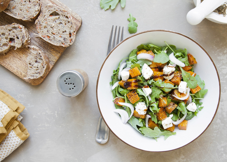 Tasty fresh salad with baked pumpkin, feta cheese, rocket and sweet red onion on brown background. Top view.の写真素材