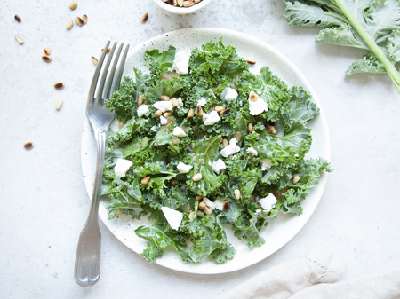 Fresh kale salad with goat cheese, pine nuts and sweet balsamic vinegar dressing with onion on grey background. Top view.の写真素材