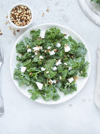 Fresh kale salad with goat cheese, pine nuts and sweet balsamic vinegar dressing with onion on grey background. Top view.の写真素材