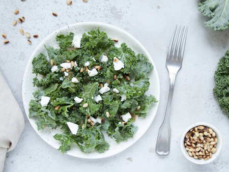Fresh kale salad with goat cheese, pine nuts and sweet balsamic vinegar dressing with onion on grey background. Top view.の写真素材