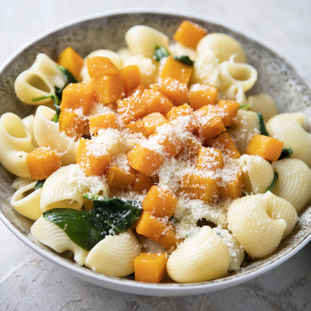 Bowl of pasta with pumpkin, spinach and cheese on shabby grey background.の写真素材
