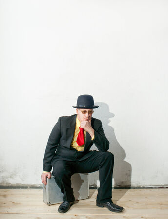 Businessman in black suit sitting on a suitcaseの写真素材