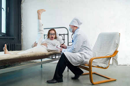 Attending doctor and crazy patient with raised leg in a hospitalの写真素材