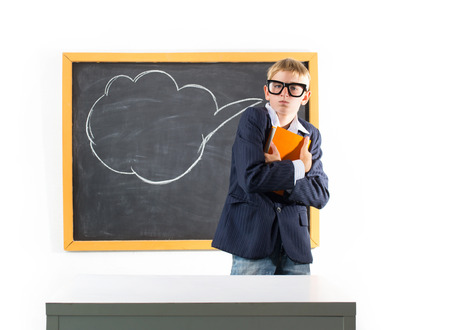 Serious schoolboy stands at the blackboard with textbookの写真素材