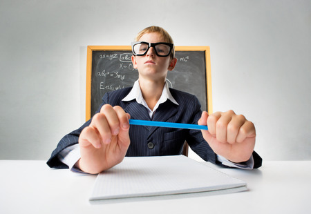 Erudite schoolboy sitting at the desk with pencilの写真素材