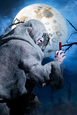Vampire in rags with syringe on the background of the moonの写真素材