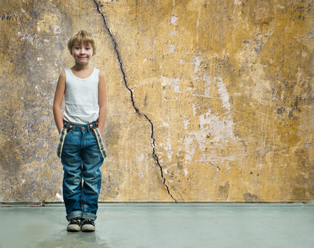 Boy in jeans stands near a wallの写真素材