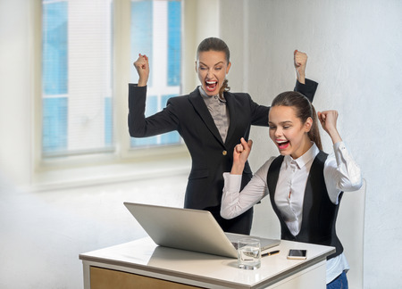 Two contented successful businesswomen work at the laptop in officeの写真素材