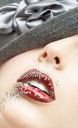Portrait of the beautiful girl with a red lipstick and with rhinestones in a black hatの写真素材
