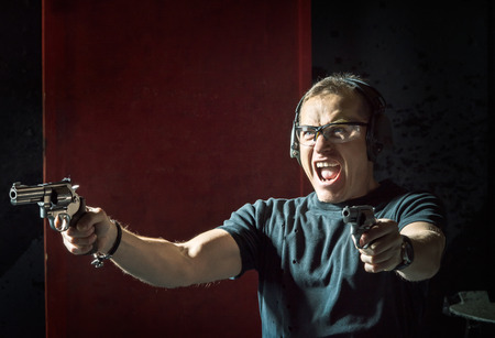 Crazy man in a headphones with a gun in his hand on the dark backgroundの写真素材