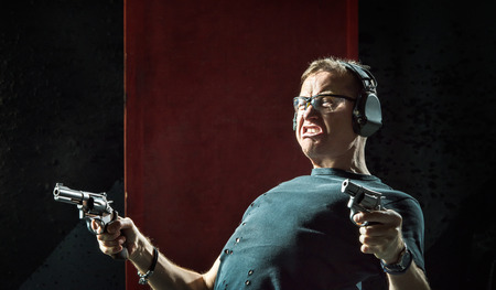 Mad man in a headphones with a gun in his hand on the dark backgroundの写真素材