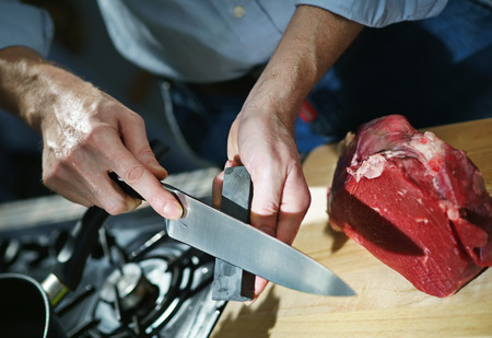 Man sharpens kitchen knife for cutting meat on the whetstoneの写真素材