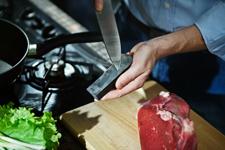 Man sharpens kitchen knife for cutting meat on the whetstoneの写真素材