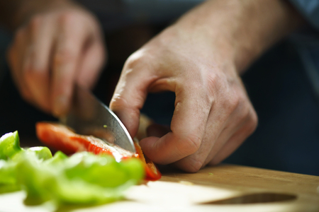 Chef cuts bell pepper with a knife on a boardの写真素材
