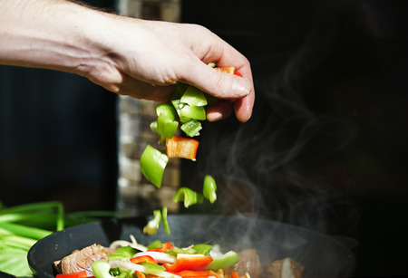 Chef puts vegetables in the frying pan with the meatの写真素材