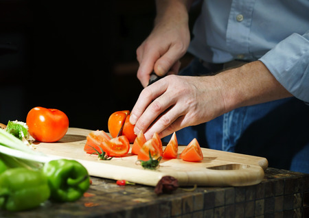 Chef cuts the tomatoes with a knife on a boardの写真素材