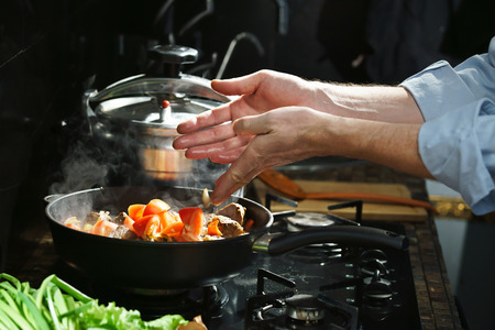 Chef puts tomatoes in the frying pan with the meatの写真素材