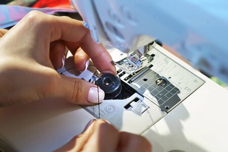 Seamstress inserts the bobbin with thread in a sewing machineの写真素材