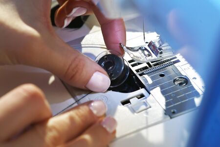 Seamstress inserts the bobbin with thread in a sewing machineの写真素材