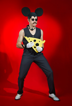 Man in a costume of a mouse with a piece of cheese in his handsの写真素材