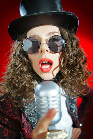 Portrait of a beautiful singer with microphone on the red backgroundの写真素材