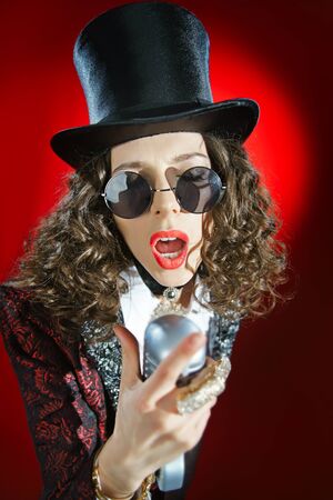 Portrait of a beautiful singer with microphone on the red backgroundの写真素材