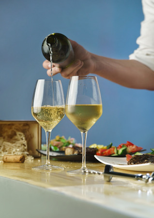 Cook pours white wine from the bottle into wine glassesの写真素材