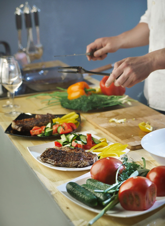 Cook lays meat steak in a plate with vegetablesの写真素材