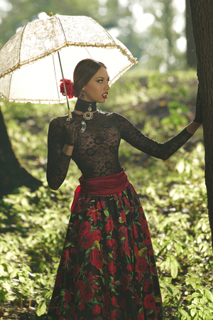 Beautiful girl in a Spanish style with a parasol near a tree in the parkの写真素材