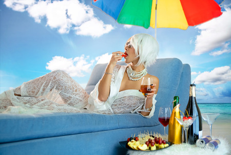 Luxurious woman on chaise lounge by the sea drinks wine with a fruitの写真素材