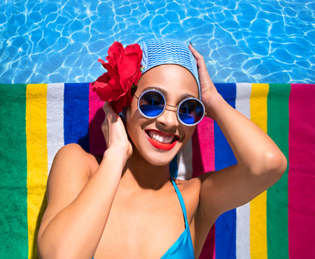 Woman in a blue swimsuit, sunglasses and  bathing cap is sunbathing on a towel by the water の写真素材