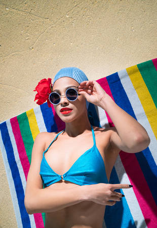 Woman in a blue swimsuit, sunglasses and  bathing cap is sunbathing on a towel on the sandの写真素材