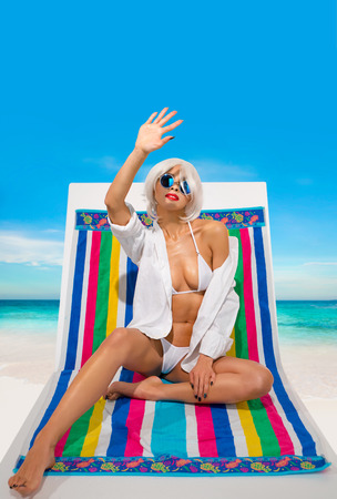Beautiful blonde girl in a white swimsuit sitting on the lounger at seaの写真素材