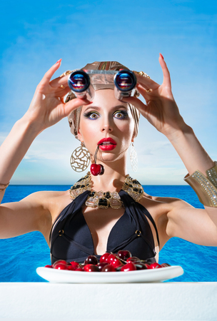 Astonished woman with a binoculars and a cherries by the seaの写真素材