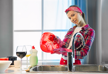 Woman in pink protective rubber gloves washes plate in the kitchenの写真素材