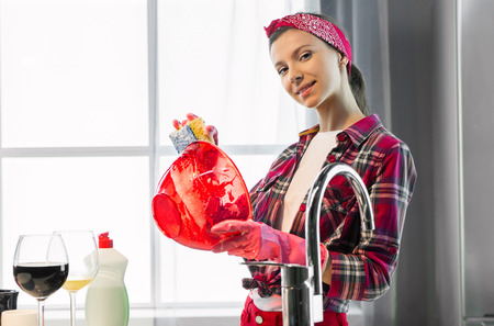 Woman in pink protective rubber gloves washes plate in the kitchenの写真素材