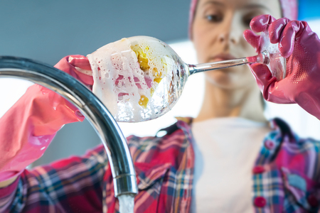 Woman in pink protective rubber gloves washes wineglass in the kitchenの写真素材
