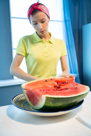 Young woman cuts watermelon with knife in the kitchenの写真素材