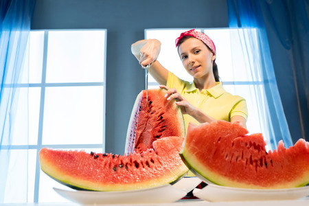 Young woman cuts watermelon with knife in the kitchenの写真素材