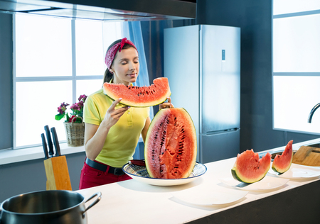 Young woman with piece of watermelon in hands in the kitchenの写真素材