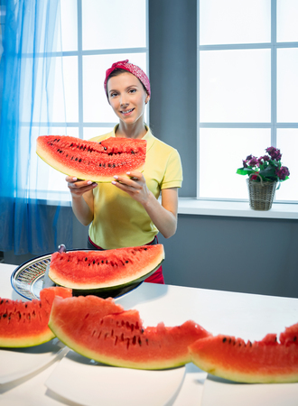 Young woman with piece of watermelon in the kitchenの写真素材
