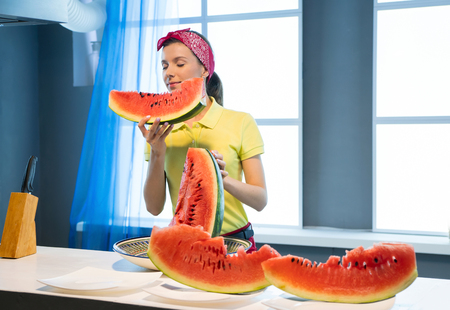 Young woman with piece of watermelon in the kitchenの写真素材
