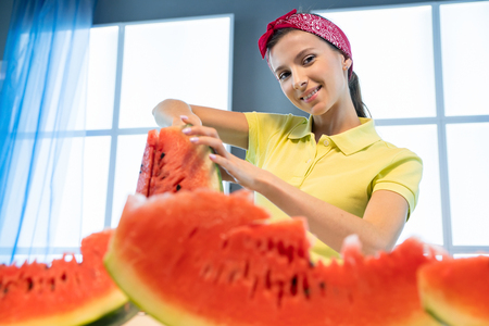 Young woman cuts watermelon with knife in the kitchenの写真素材