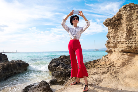 Beautiful woman with mobile phone on rocky seashoreの写真素材